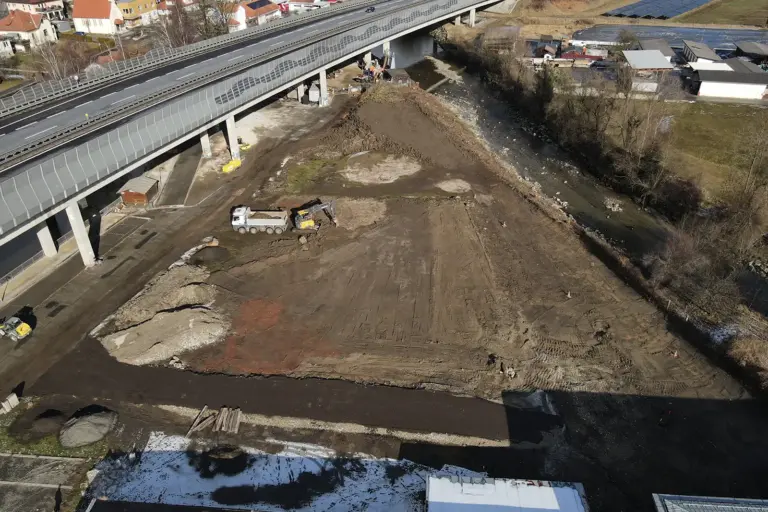 Ein großer Platz mit Erde von oben. Links ist eine Straße und rechts ein Fluss erkennbar.
