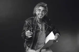 Ein Mann mit zirka schulterlangen Haaren und Fünftagebart in Lederjacke mit Skizzenblock und Stift in Händen