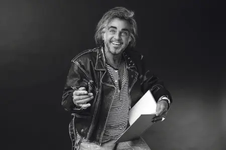 Ein Mann mit zirka schulterlangen Haaren und Fünftagebart in Lederjacke mit Skizzenblock und Stift in Händen