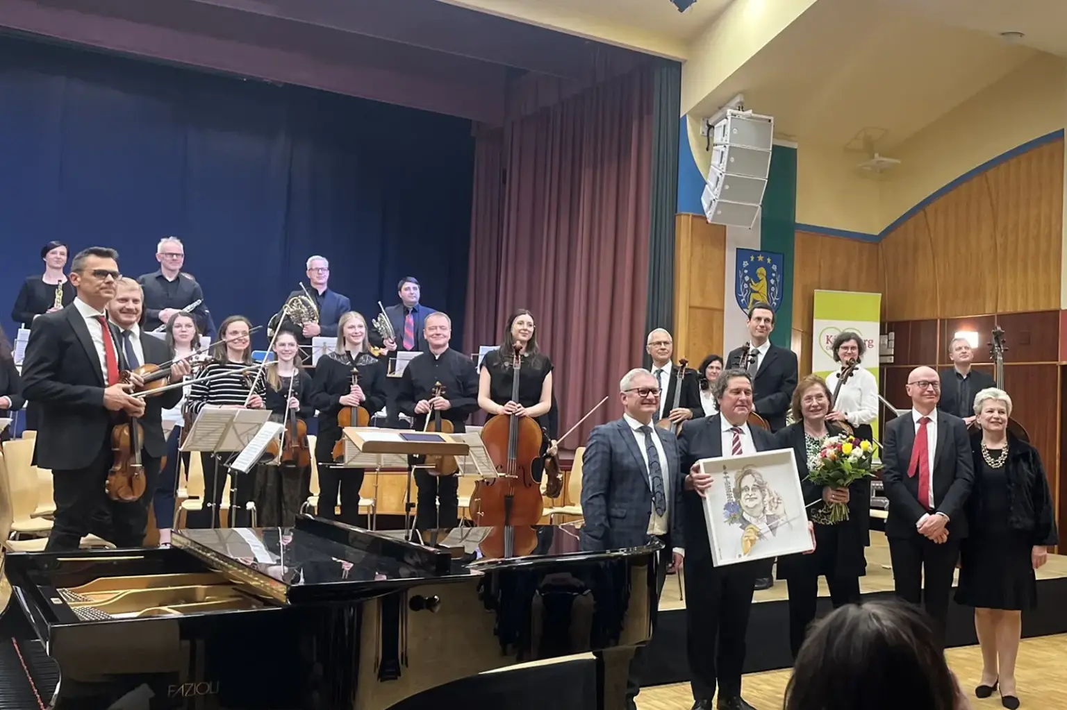 Eine Gruppe von Musikern und wetere Personen stehen auf und vor einer Bühne
