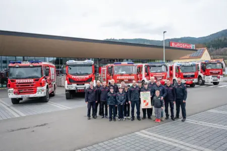 Eine Gruppe von Personen in Uniform steht auf einem Parkplatz mit Feuerwehrautos vor einem Geschäft