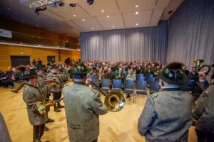 Eine Jagdhornbläsergruppe in jagdlicher Tracht spielt in einem mit rund 300 Zuhörern besetzten Saal