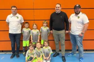 Drei Männer und sechs Kinder stehen bzw. sitzen vor einer Wand.