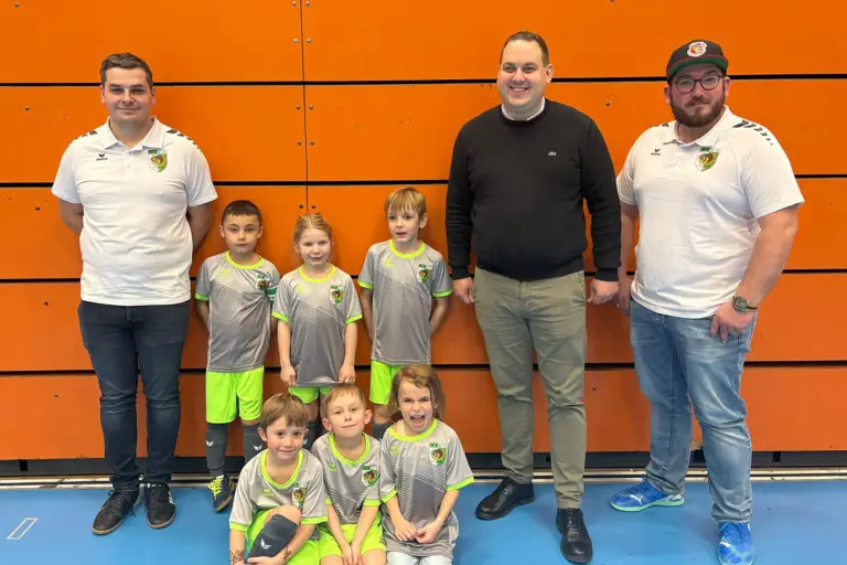 Drei Männer und sechs Kinder stehen bzw. sitzen vor einer Wand.