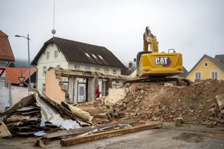 Ein Bagger steht auf einem Schutthaufen, daneben sind noch die letzte Reste eines Gebäudes zu sehen.