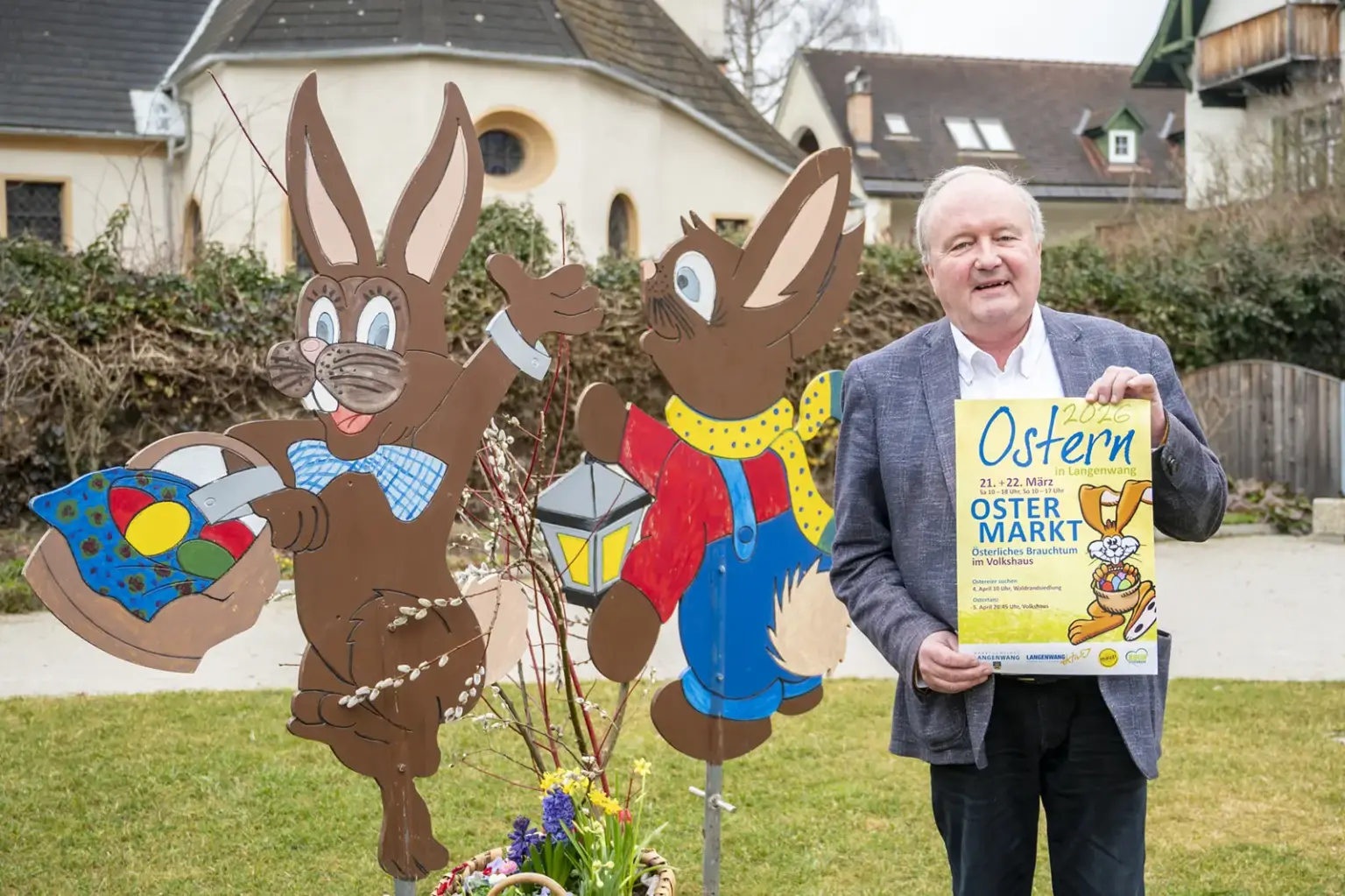 Österliches Brauchtum in Langenwang Ein Mann steht mit einem Plakat in der Mann neben zwei großen aus Holz bestehenden Osterhasen.