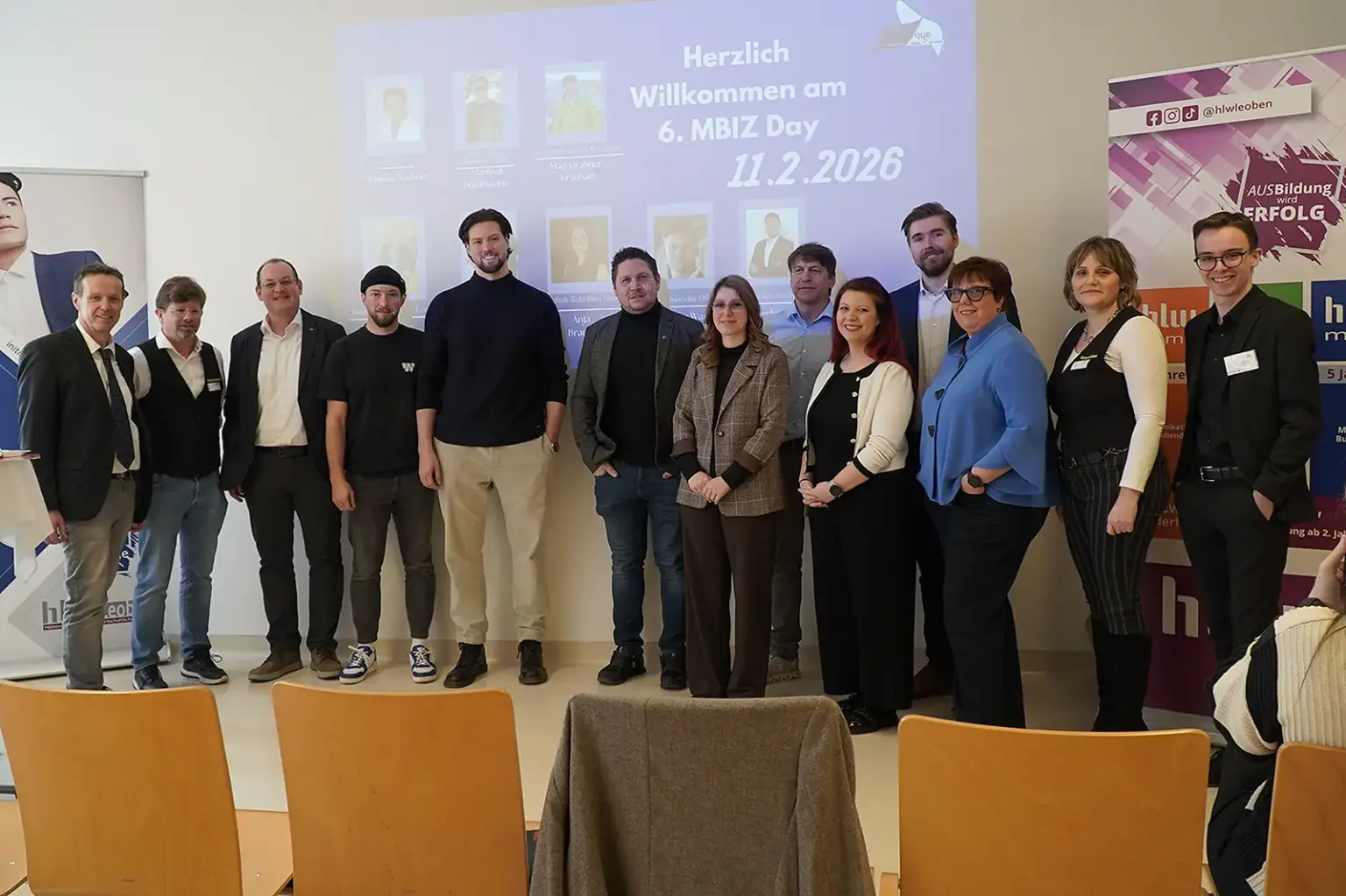 Ein Wirtschaftstag an der HLW Leoben Ein Gruppe von Menschen stehen nebeneinander in einem Raum. Hinter ihnen an der Wand ist eine Präsentation zu sehen. Vor ihnen stehen Sesseln.