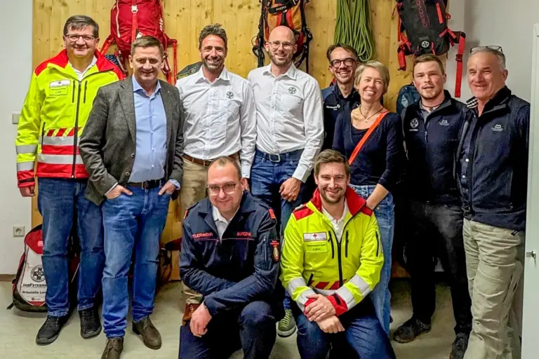 Eine Gruppe von Personen steht vor einer Wand mit Rucksäcken und Seilen