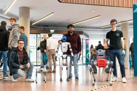 Drei Männer stehen mit Robotern in einer Halle