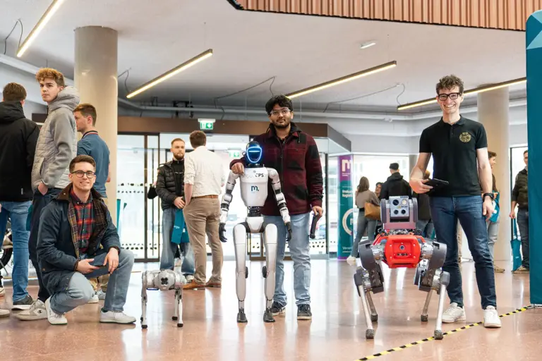 Drei Männer stehen mit Robotern in einer Halle