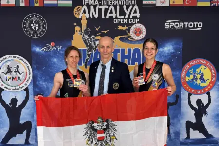 Zwei Damen mit Medaillen und ein Mann halten gemeinsam eine Österreich-Fahne.