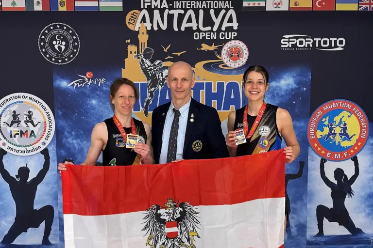 Zwei Damen mit Medaillen und ein Mann halten gemeinsam eine Österreich-Fahne.