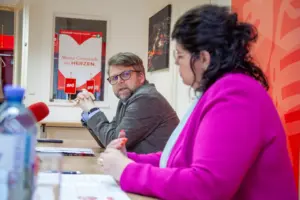 Eine Frau und ein Mann sitzen an einem Tisch, vor ihnen ein Mikrofon