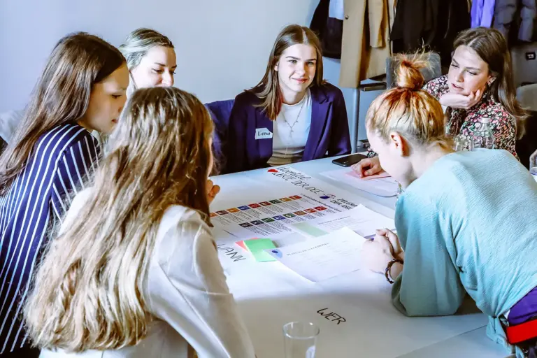 Sechs Jugendliche sitzen um einen mit Papieren bedeckten Tisch