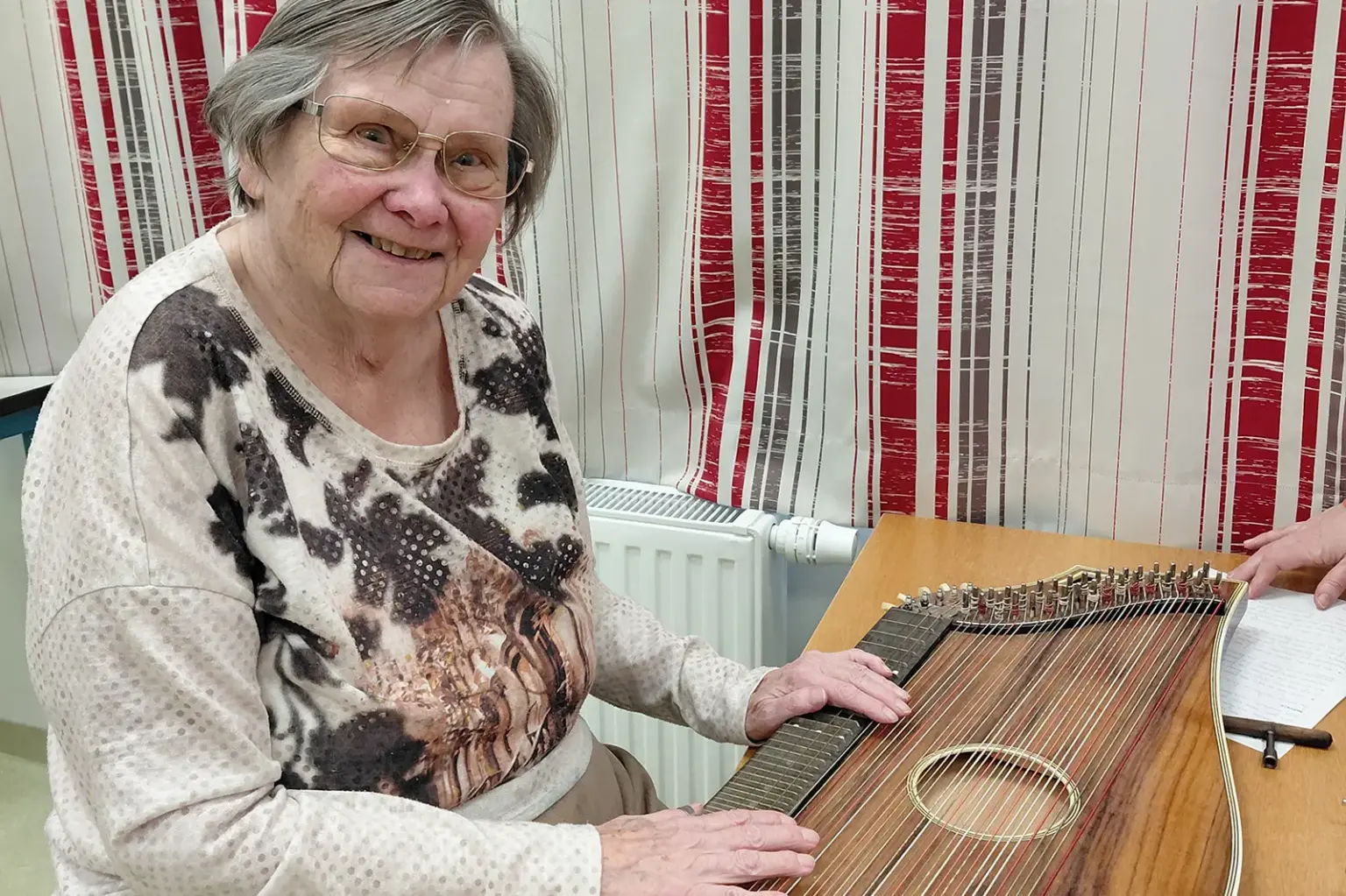 Eine ältere Frau sitzt mit einer Zither an einem Tisch