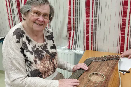 Eine ältere Frau sitzt mit einer Zither an einem Tisch