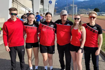 Ein Gruppe von Menschen stehen neben einander, dahinter ist ein Stadion und eine Laufbahn zu erkennen.