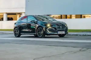 Ein schwarzes Auto der Kompaktklasse fährt auf einer Straße von links nach rechts, im Hintergrund eine Betonwand