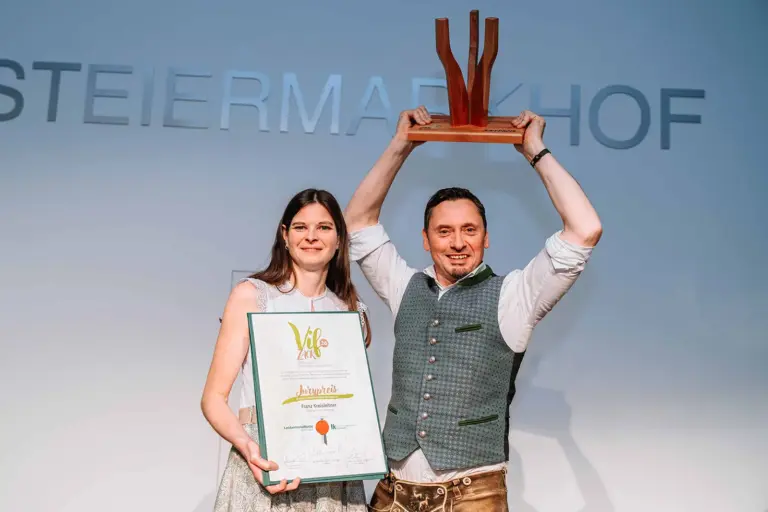 Ein Mann und eine Frau halten eine Urkunde und eine Trophäe