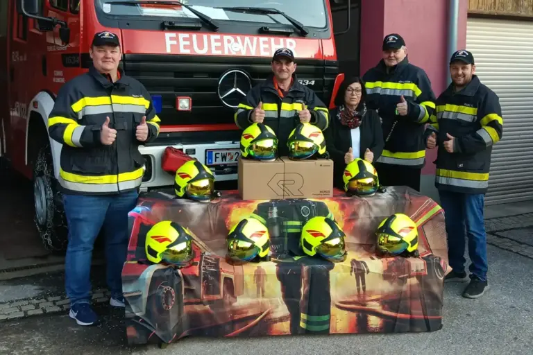 Vier Männer in Uniform und eine Frau hinter einem Tisch voller gelber Helme