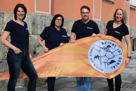 Vier Menschen stehen nebeneinander und halten gemeinsam eine Beachflag.