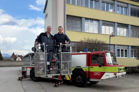 Die Störche können kommen Zwei Männer im Hebekorb eines alten Feuerwehrfahrzeuges vor einem Haus