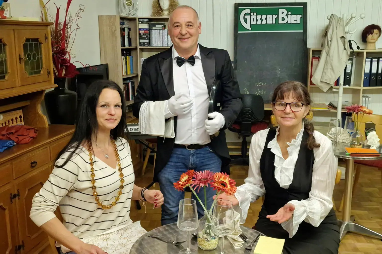 Zwei Frauen werden an einem Kaffeehaustisch von einem Kellner bedient