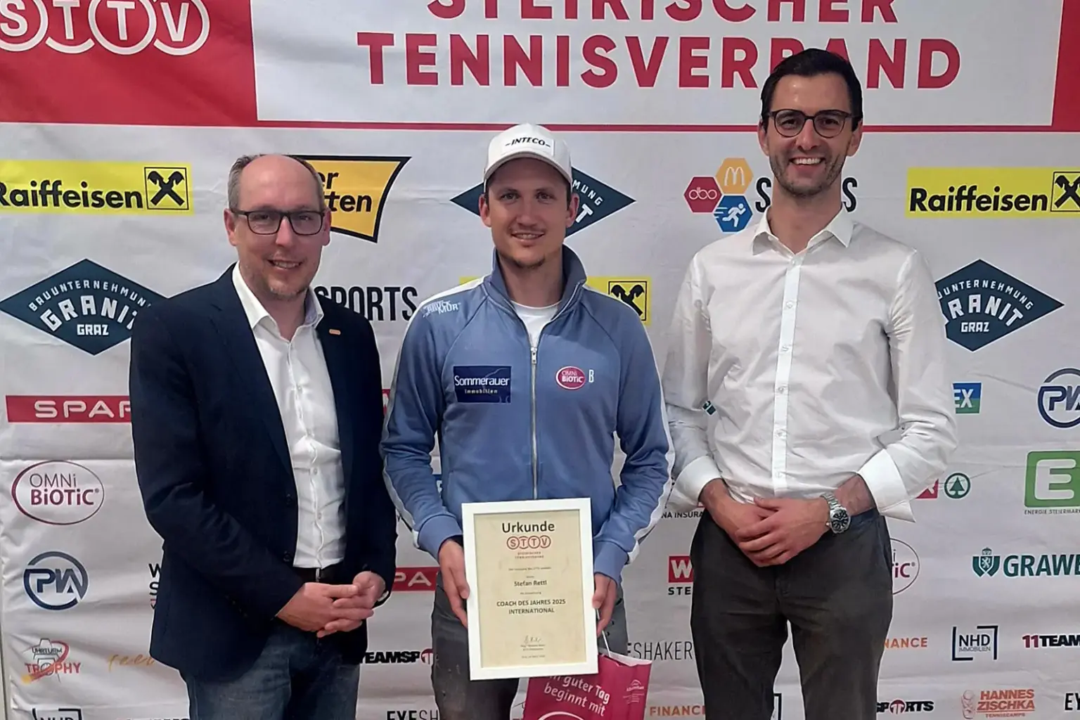 Drei Männer stehen nebeneinander, der mittlere hat eine Urkunde in der Hand.