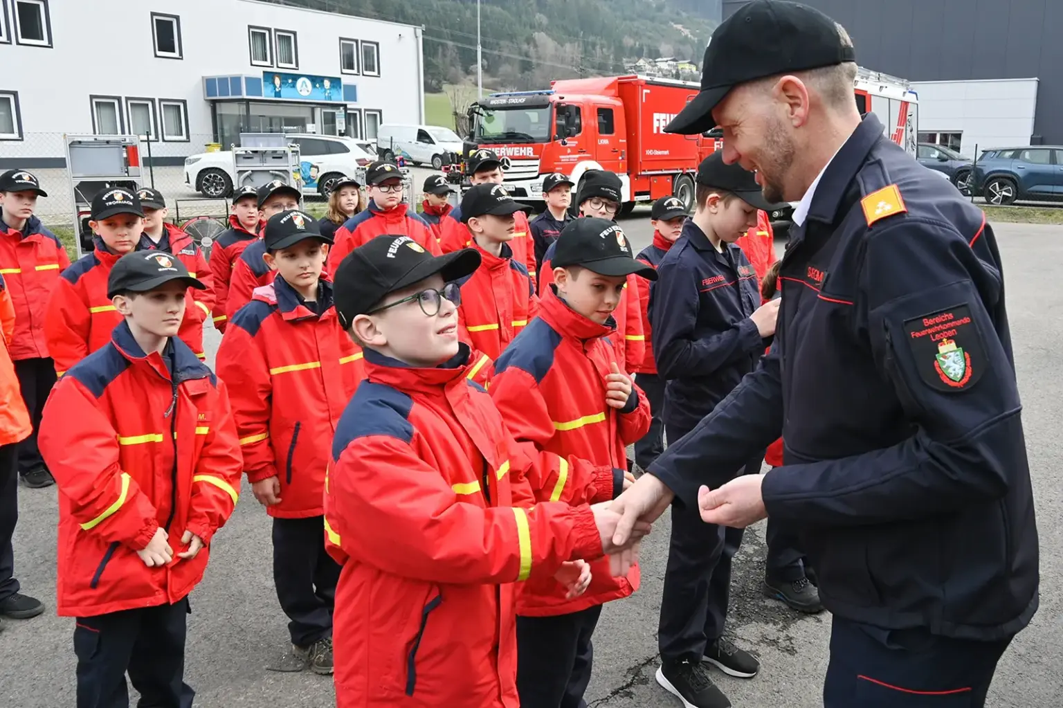 Ein Mann in Uniform gratuliert einer großen Gruppe von Kindern und Jugendlichen in roten Jacken