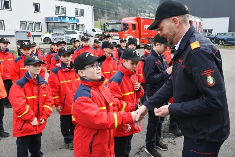 Ein Mann in Uniform gratuliert einer großen Gruppe von Kindern und Jugendlichen in roten Jacken