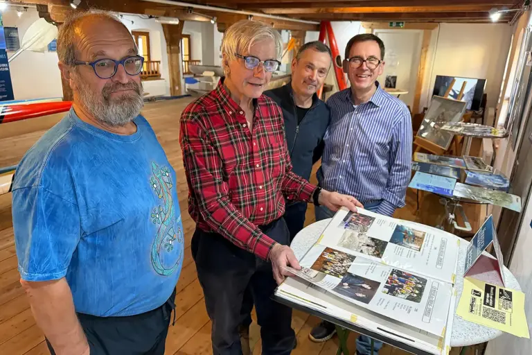 Die Skijak-Schau zieht weiter Vier Männer blättern in einem großen Buch mit vielen Bildern