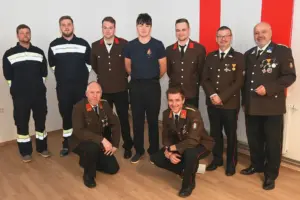 Neun Männer in Uniform stehen und hocken vor einer Wand