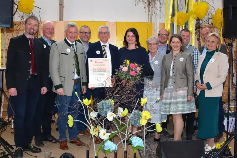 Zwölf Personen, großteils in Tracht gekleidet, auf einer dekorierten Bühne