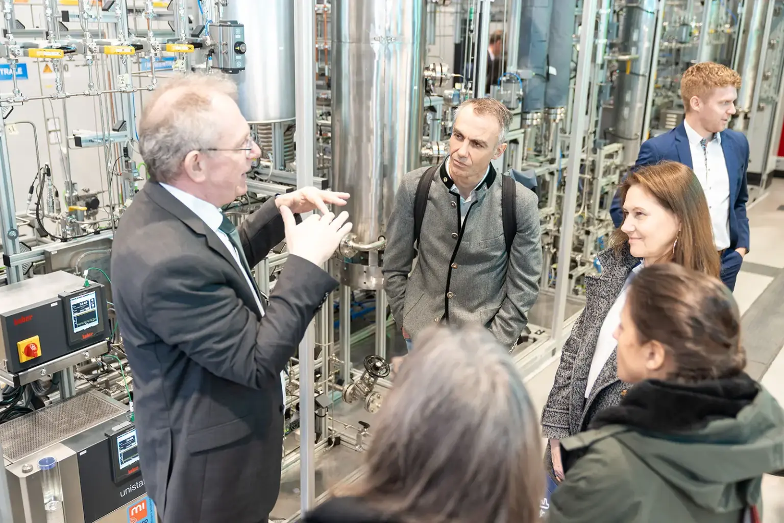 Eine Gruppe Menschen vor einer komplex anmutenden technische Anlage mit vielen Behältern und Leitungen