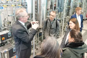 Eine Gruppe Menschen vor einer komplex anmutenden technische Anlage mit vielen Behältern und Leitungen