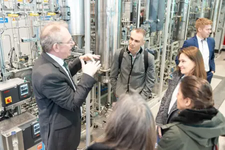 Eine Gruppe Menschen vor einer komplex anmutenden technische Anlage mit vielen Behältern und Leitungen