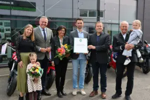 Gruppenfoto bei einer feierlichen Urkundenverleihun. Im Hintergrund stehen Motorräder.