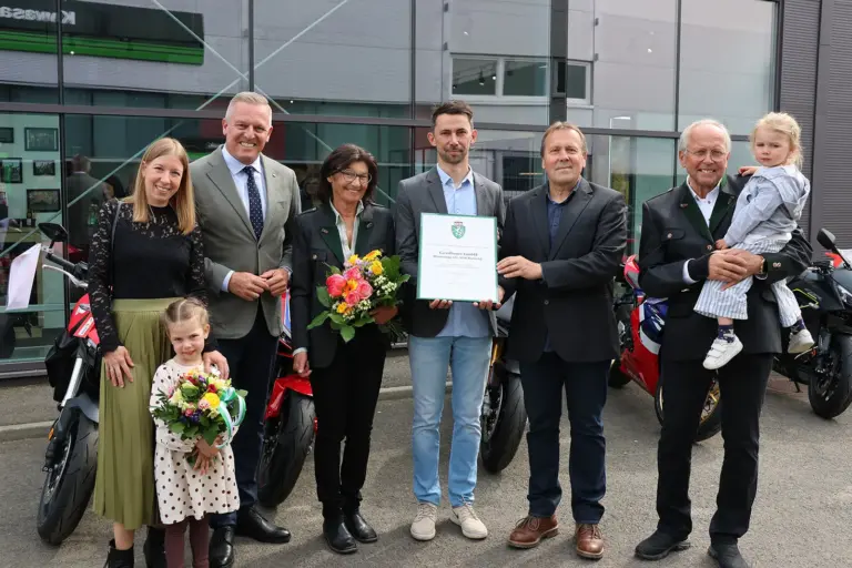 Gruppenfoto bei einer feierlichen Urkundenverleihun. Im Hintergrund stehen Motorräder.