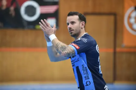 Ein Handballspieler in blauem Trikot klatscht während eines Spiels in einer Sporthalle in die Hände.