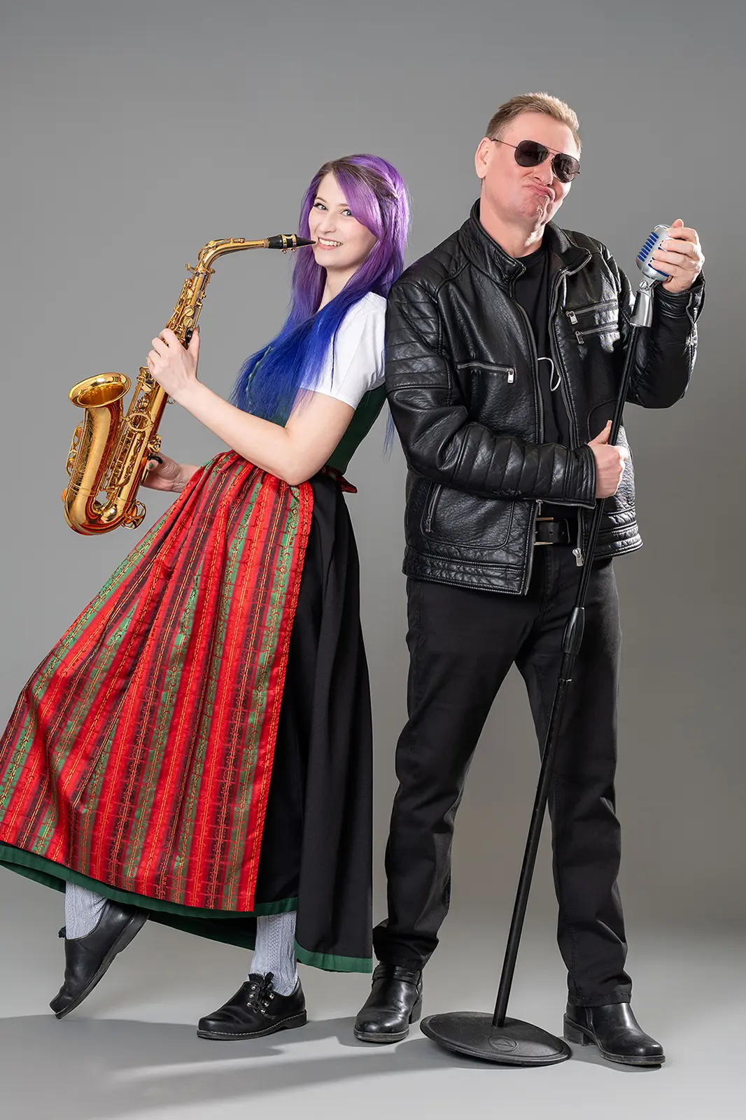 Eine junge Frau im Dirndl mit einem Saxophon steht neben einem Mann in einer Lederjacke
