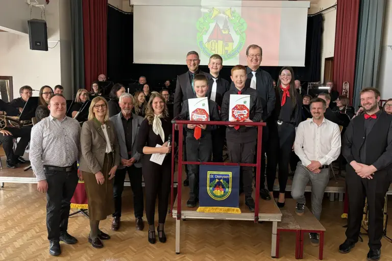 Zwei Buben präsentieren gemeinsam mit mehreren erwachsenen Personen Urkunden