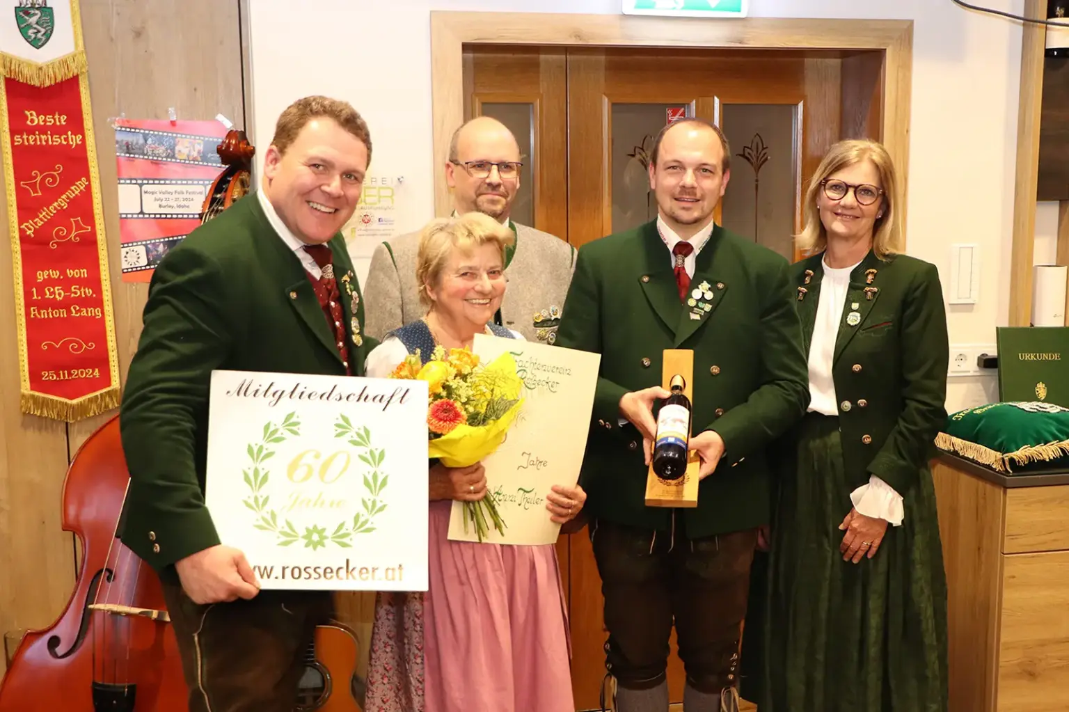 Drei Männer und zwei Frauen in Tracht halten Blumen, Geschenke und Urkunden