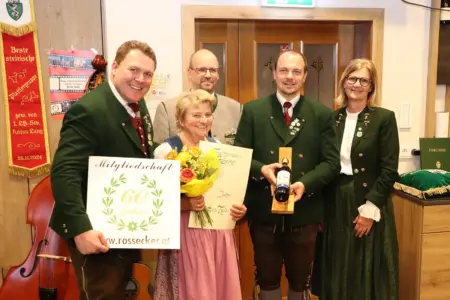 Drei Männer und zwei Frauen in Tracht halten Blumen, Geschenke und Urkunden