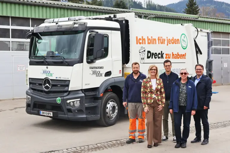 Drei Männer und zwei Frauen stehen neben einem Müllfahrzeug