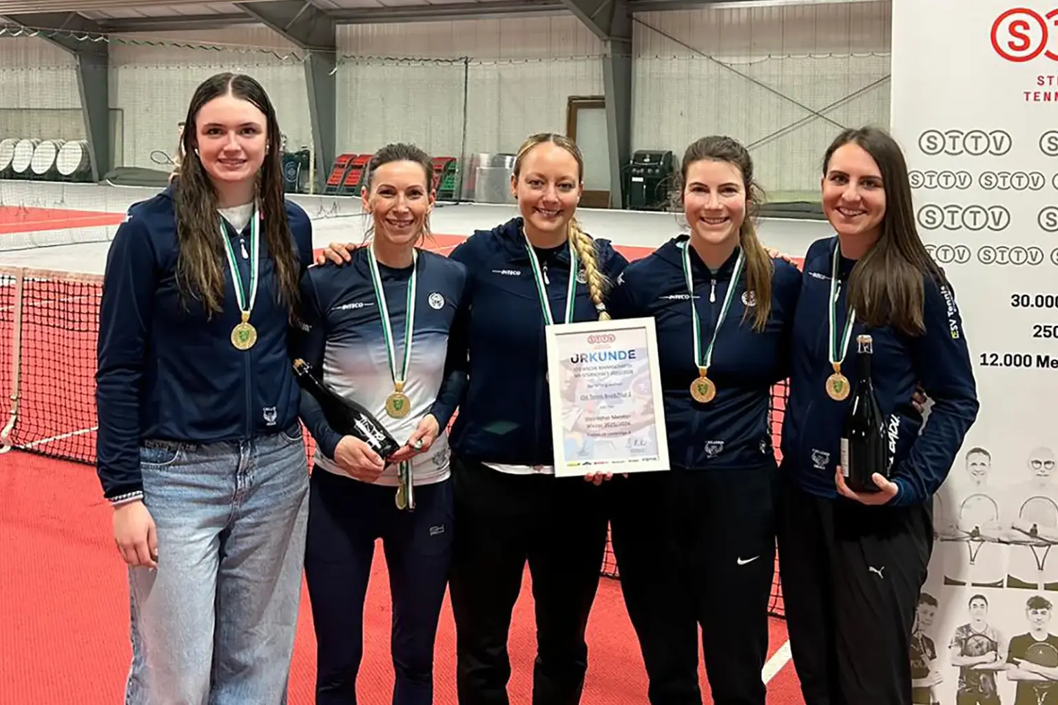 Fünf Damen stehen mit Medaillen und einer Urkunde in einer Tennishalle.