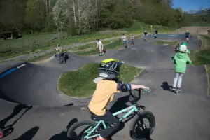Kinder mit Helmen fahren mit Fahrrädern und Rollern auf einer asphaltierten Buckelbahn