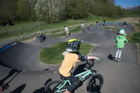 Kinder mit Helmen fahren mit Fahrrädern und Rollern auf einer asphaltierten Buckelbahn