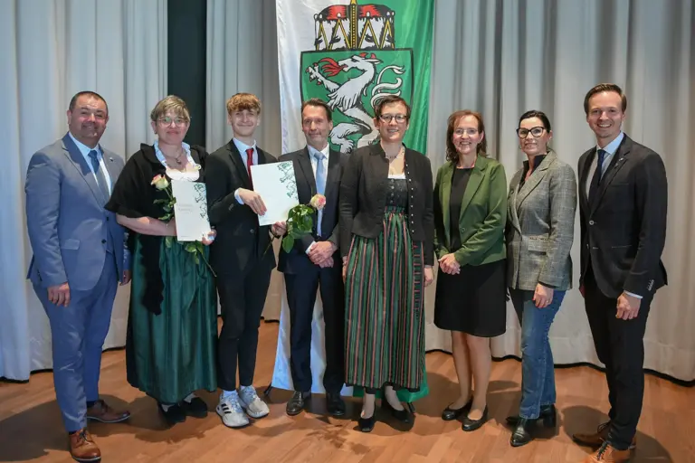 Acht Personen stehen mit Urkunden vor einer Steiermarkfahne