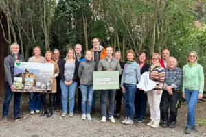 Eine Gruppe von Personen steht mit Plakaten und Prospekten vor einer Baumreihe