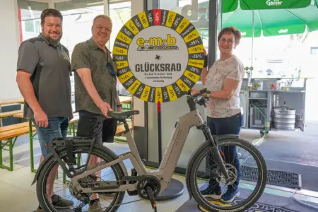 Zwei Männer und eine Frau stehen mit einem E-Bike vor einem Glücksrad der Firma EMB.